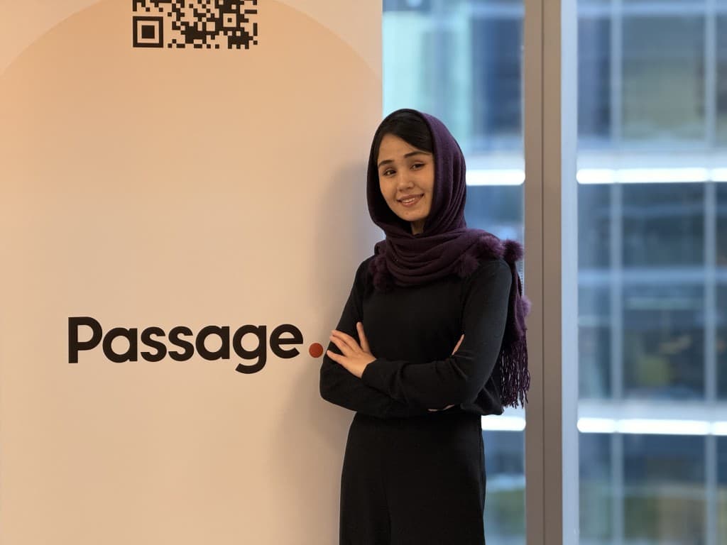 An Afghan woman standing beside the Passage brand mark at the Passage office in Toronto